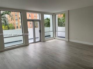 An empty living room with light wood-look flooring and large windows overlooking a balcony — 700 Biltmore Way # 219, Coral Gables FL 33134, CORAL GABLES, FL