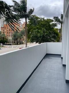 A balcony with a gray floor and white walls overlooks a street with palm trees — 700 Biltmore Way # 219, Coral Gables FL 33134, CORAL GABLES, FL