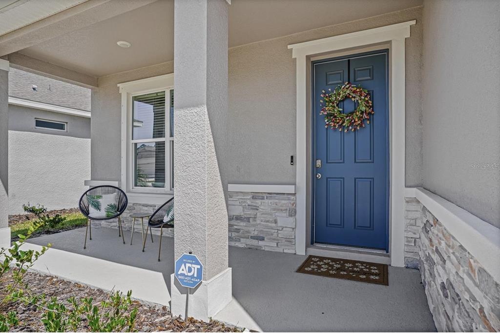A front porch features a blue door, stone veneer accents, and two modern chairs — 17925 FATTORIA TERRACE, LAKEWOOD RANCH, FL