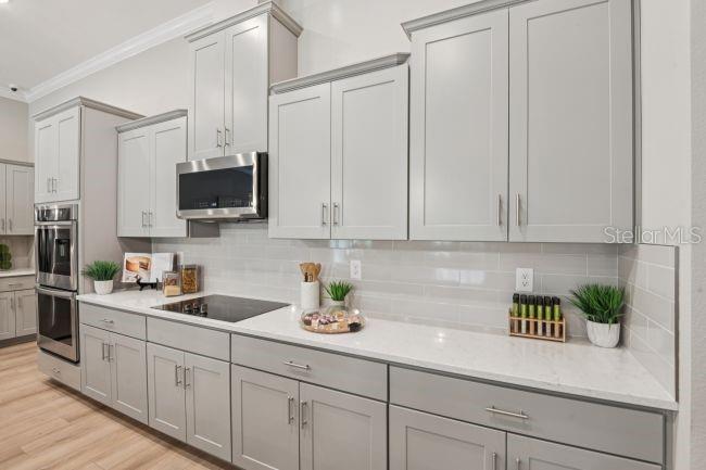 A modern kitchen features light gray cabinets, white countertops, stainless steel appliances, and subway tile — 17041 ROYAL PALMS DRIVE, GROVELAND, FL