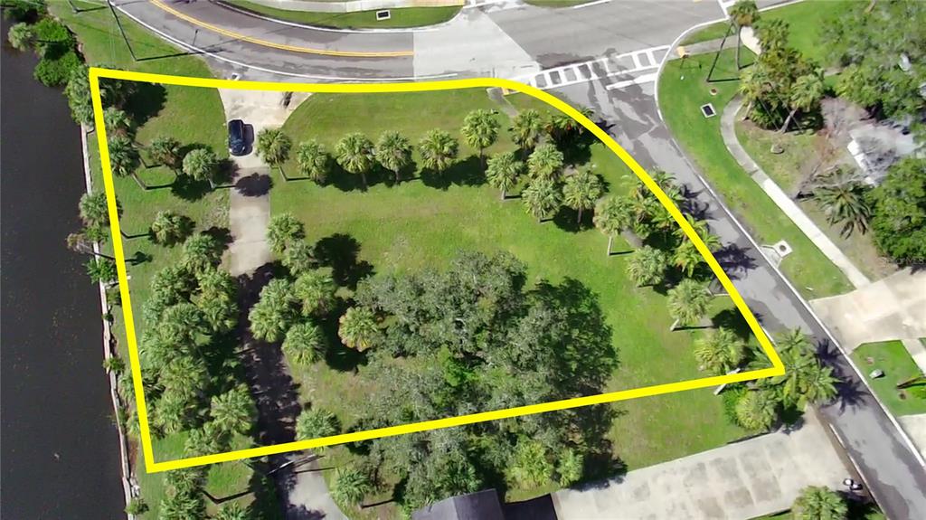 An aerial view shows a vacant, grassy corner lot outlined in yellow next to a canal — PARK AVENUE, TARPON SPRINGS, FL