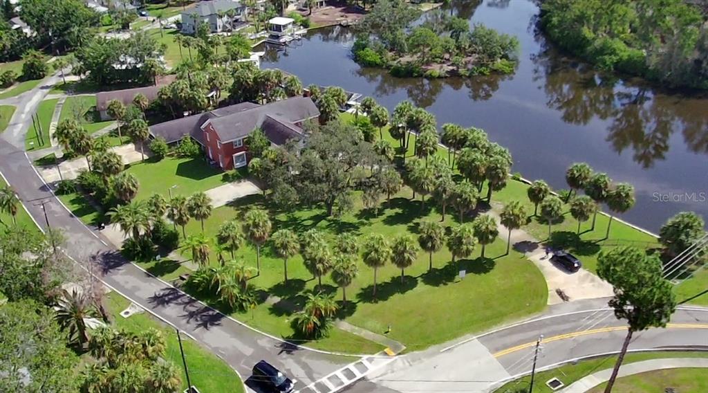 An aerial view shows a red brick house situated on a large, palm-filled waterfront lot — PARK AVENUE, TARPON SPRINGS, FL