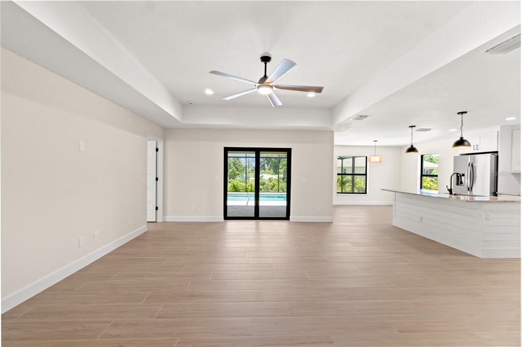 An open-concept living area features light wood-look tile flooring, a tray ceiling, and a kitchen — 196 ARCH DRIVE, ROTONDA WEST, FL