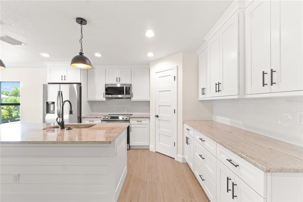A modern kitchen features white cabinets, granite countertops, stainless steel appliances, and a central island — 196 ARCH DRIVE, ROTONDA WEST, FL