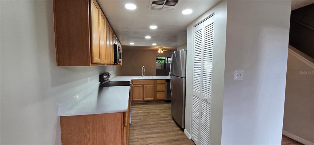 A kitchen features wood cabinets, stainless steel appliances, and light-colored countertops over wood-look flooring — 1834 FOXHALL CIRCLE, KISSIMMEE, FL