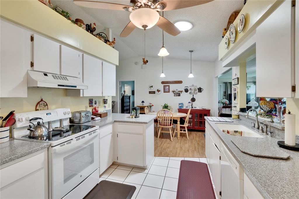 A kitchen with white cabinets, granite-look countertops, and a dining area in the background — 3154 PRAIRIE DUNES CIRCLE W, LAKELAND, FL