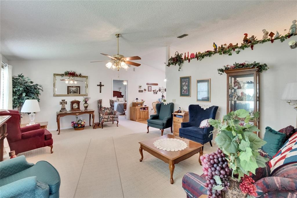 A living room features beige carpeting, multiple armchairs, a wooden coffee table, and decorative wall accents — 3154 PRAIRIE DUNES CIRCLE W, LAKELAND, FL