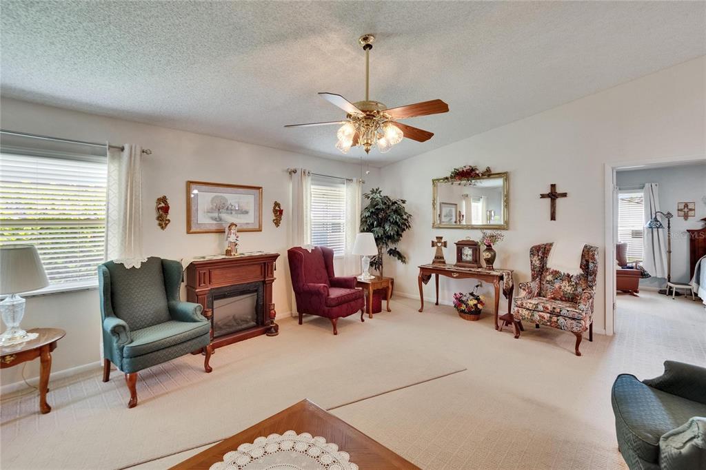A living room features a fireplace, several armchairs, a ceiling fan, and beige carpeting — 3154 PRAIRIE DUNES CIRCLE W, LAKELAND, FL