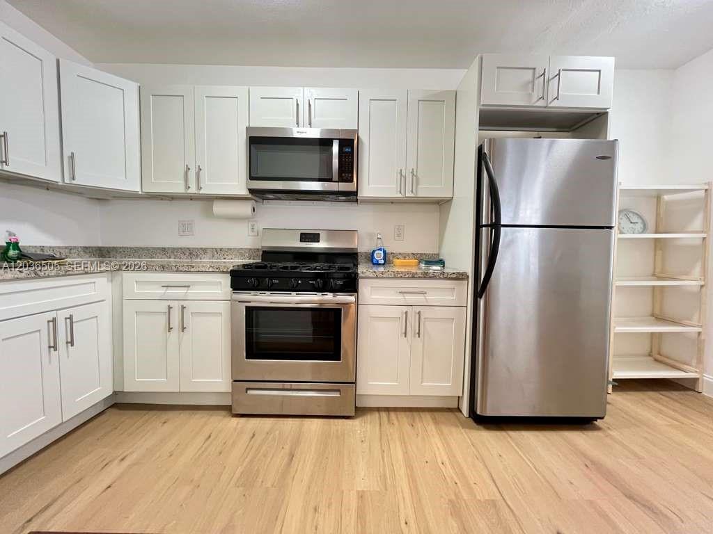 A kitchen features white cabinets, stainless steel appliances, granite countertops, and light wood flooring — 7928 Harding Ave # 3, Miami Beach FL 33141, MIAMI BEACH, FL