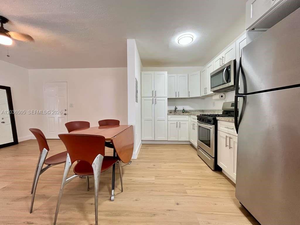 A kitchen with white cabinets and stainless steel appliances sits beside a dining area — 7928 Harding Ave # 3, Miami Beach FL 33141, MIAMI BEACH, FL