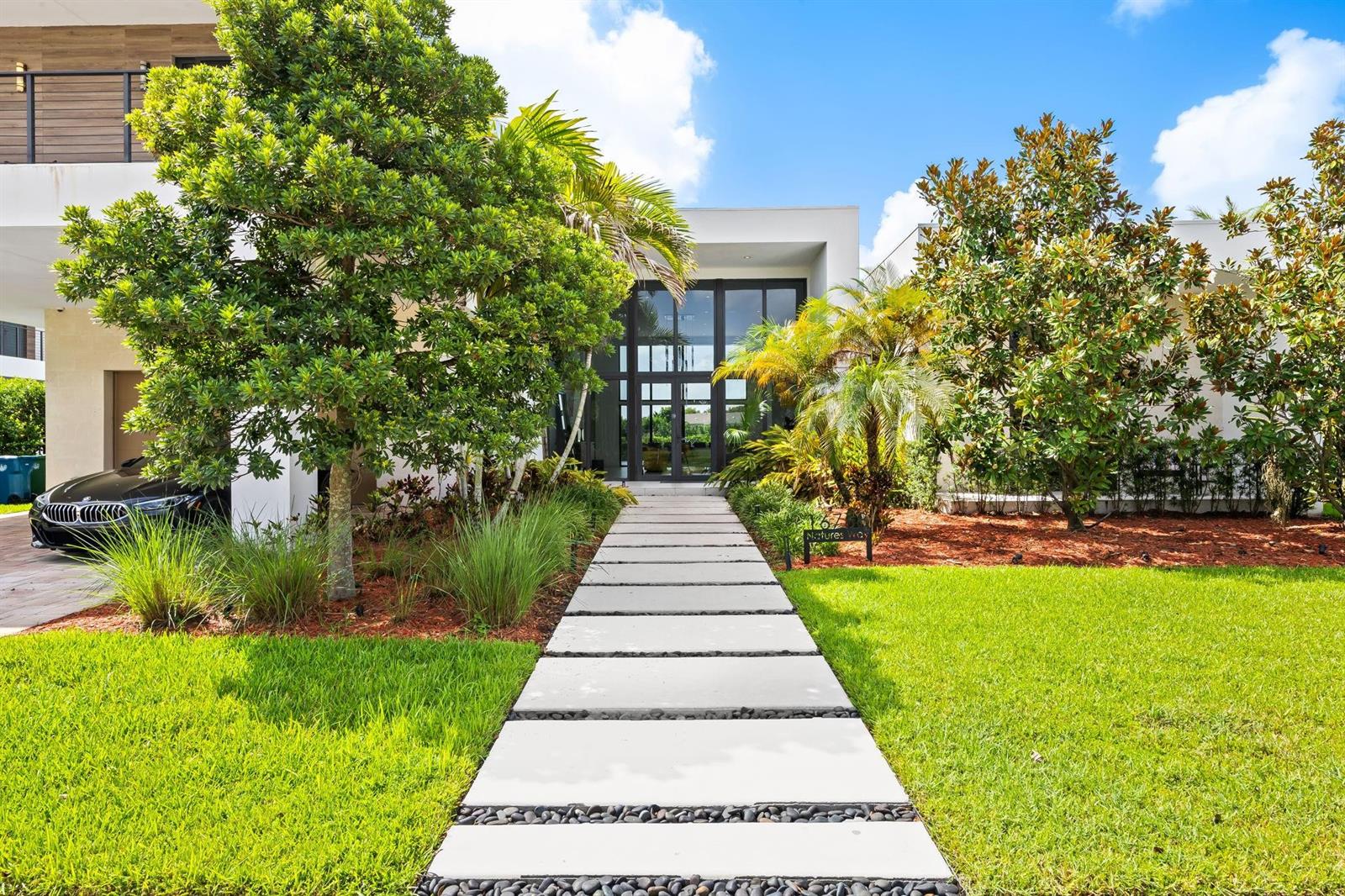 A modern house exterior features a concrete paver walkway leading to a glass-paneled front entrance — 16768 Natures Way, Weston FL 33326, WESTON, FL