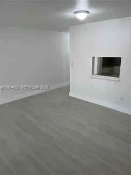 An empty room with light gray wood-look flooring, white walls, and a small pass-through window — 20922 NW 39th Ave, Miami Gardens FL 33055, MIAMI GARDENS, FL