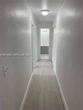 A narrow hallway with white walls and light wood-look flooring leads to a bathroom — 20922 NW 39th Ave, Miami Gardens FL 33055, MIAMI GARDENS, FL