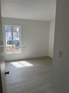 An empty room features light-colored wood-look flooring, white walls, and a window overlooking a street — 20922 NW 39th Ave, Miami Gardens FL 33055, MIAMI GARDENS, FL