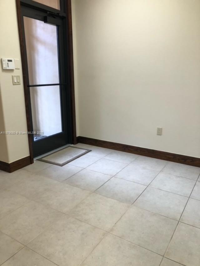A room with light-colored tile flooring, white walls, dark wood trim, and a glass door — 35 Almeria Ave, Coral Gables FL 33134, CORAL GABLES, FL