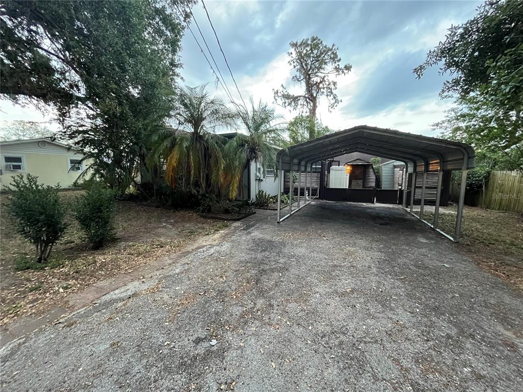 A metal carport stands on a paved driveway in front of a single-story house — 5325 LIME AVENUE, SEFFNER, FL
