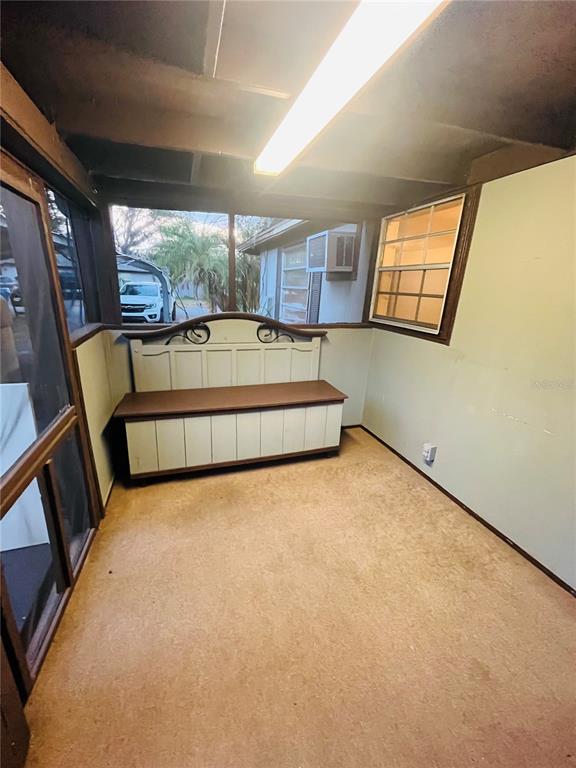 A screened-in porch features a wooden storage bench, beige carpeting, and a window unit — 5325 LIME AVENUE, SEFFNER, FL