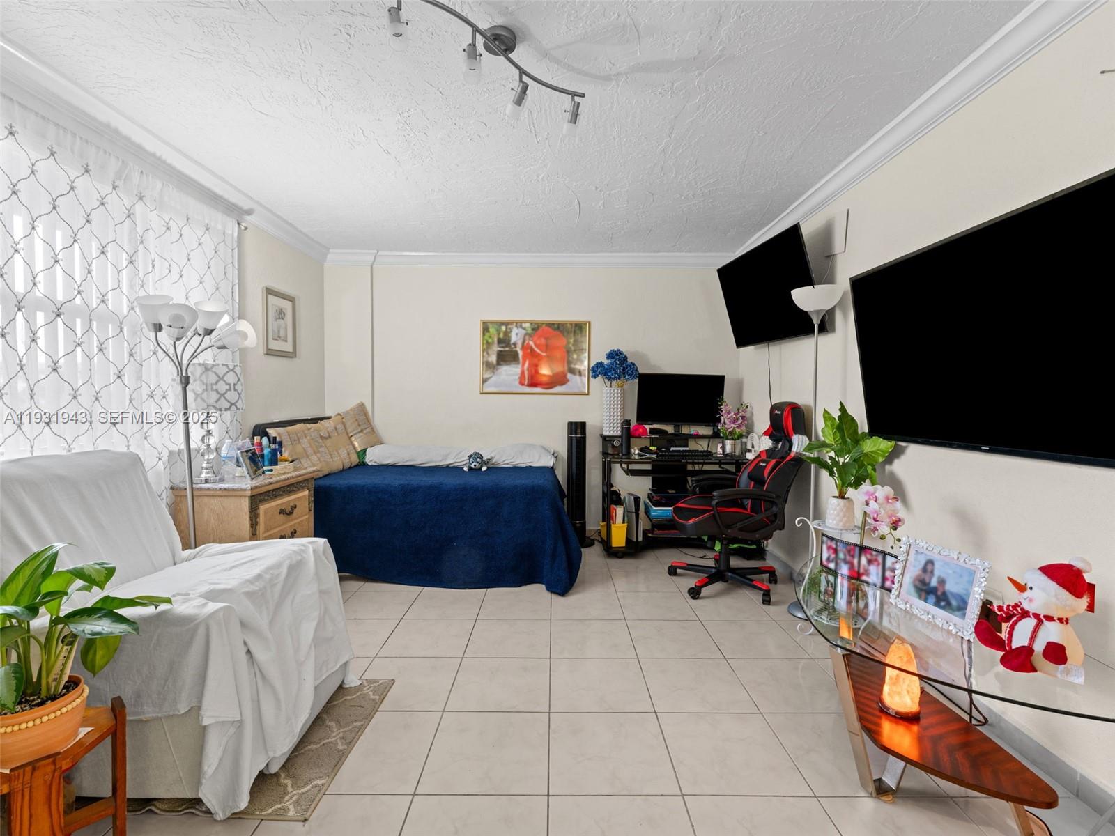 A bedroom with tile floors, a bed, a desk with a gaming chair, and televisions — 1655 W 44th Pl # 448, Hialeah FL 33012, HIALEAH, FL