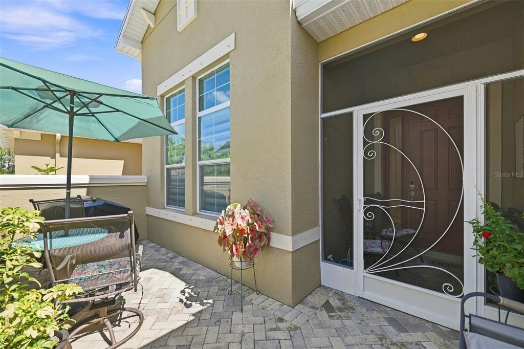 A paved patio features a patio umbrella, outdoor furniture, and a screened-in entryway door — 2109 SIFIELD GREENS WAY UNIT 70, SUN CITY CENTER, FL