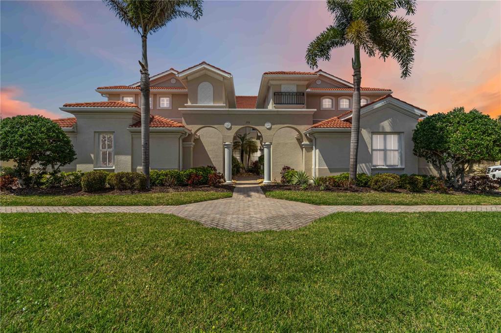 A two-story Mediterranean-style house with a tiled roof, arched entryway, and two tall palm trees — 133 BELLA VISTA TERRACE UNIT 32C, NORTH VENICE, FL