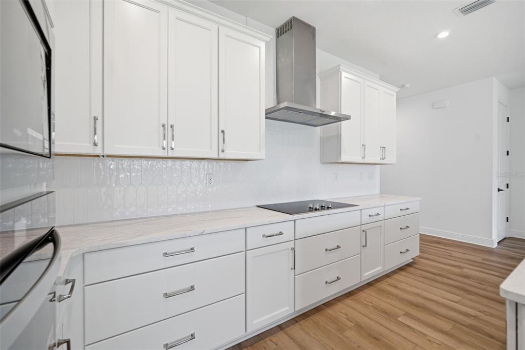 A modern kitchen features white cabinets, light countertops, a stainless steel range hood, and wood flooring — 11834 RICHMOND TRAIL, PARRISH, FL