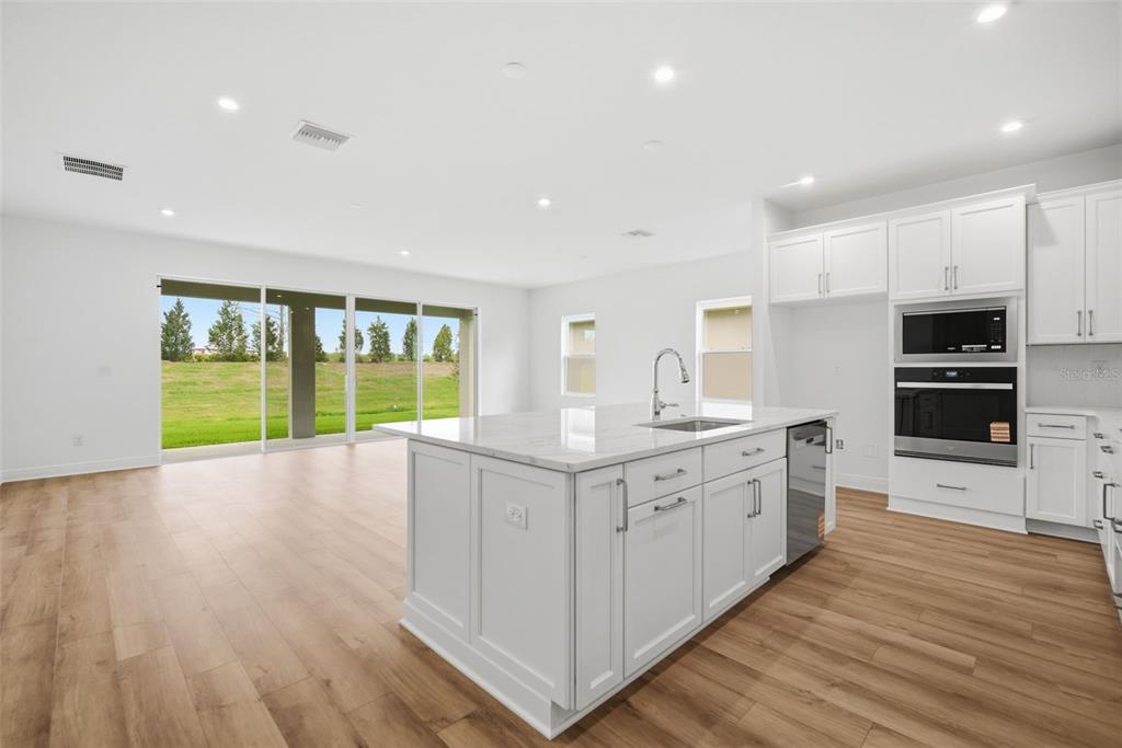 A bright kitchen with a white island, stainless appliances, and wood-look flooring overlooking a yard — 11834 RICHMOND TRAIL, PARRISH, FL