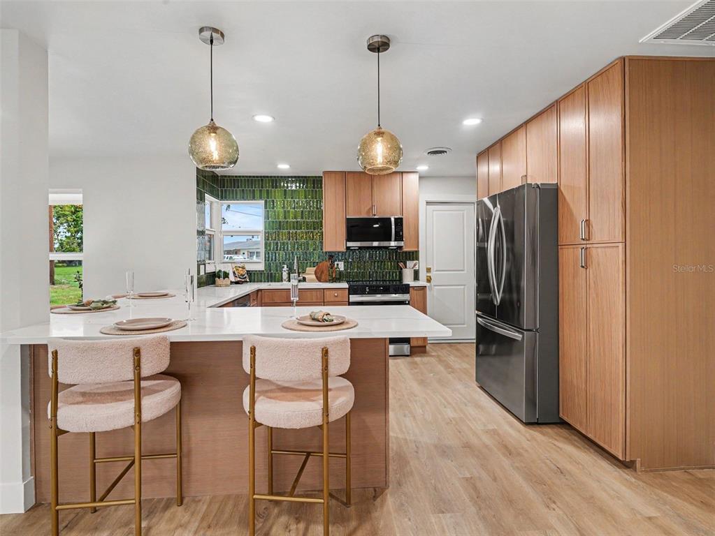 A kitchen features light wood cabinets, a green tiled backsplash, and a white peninsula island — 9911 ROYAL PALM DRIVE, BRADENTON, FL