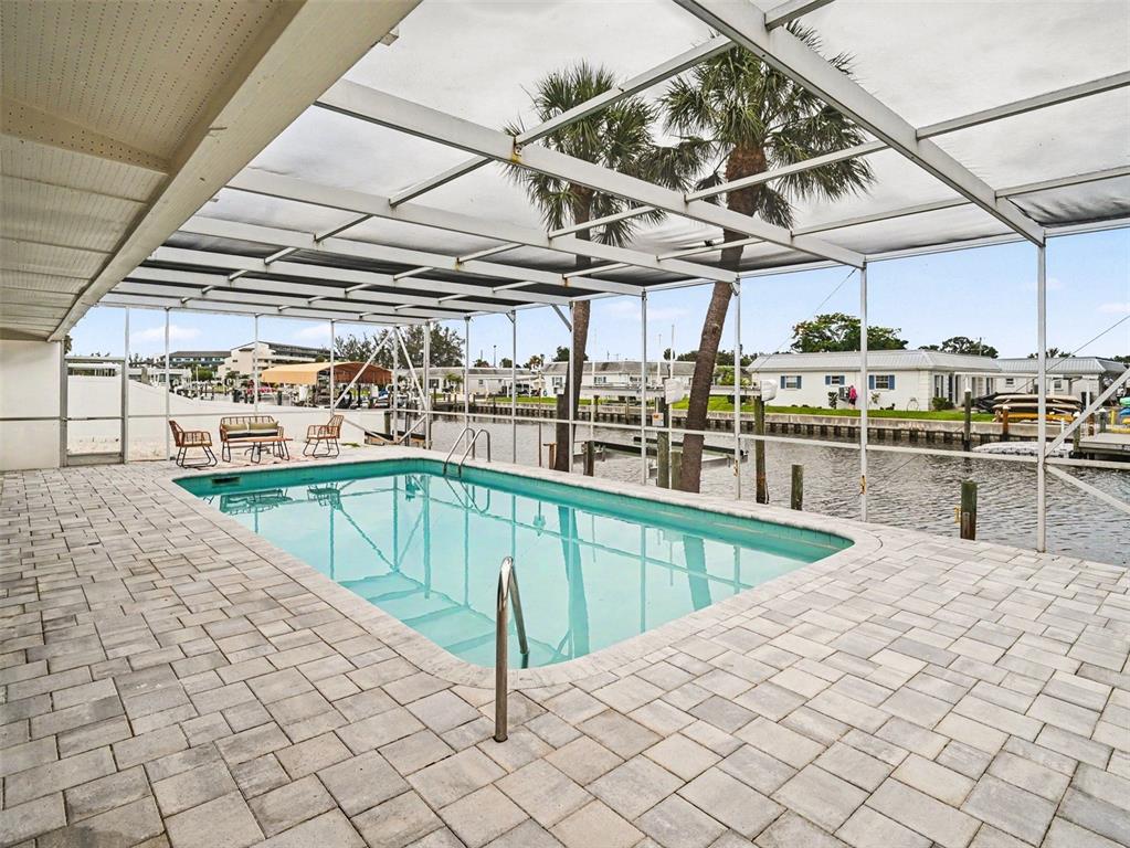 A screened-in swimming pool with a paver deck overlooks a canal with boat docks — 9911 ROYAL PALM DRIVE, BRADENTON, FL