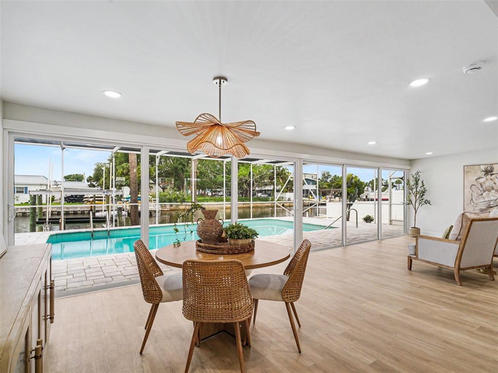 A dining area with a wicker chandelier overlooks a swimming pool and canal through glass doors — 9911 ROYAL PALM DRIVE, BRADENTON, FL