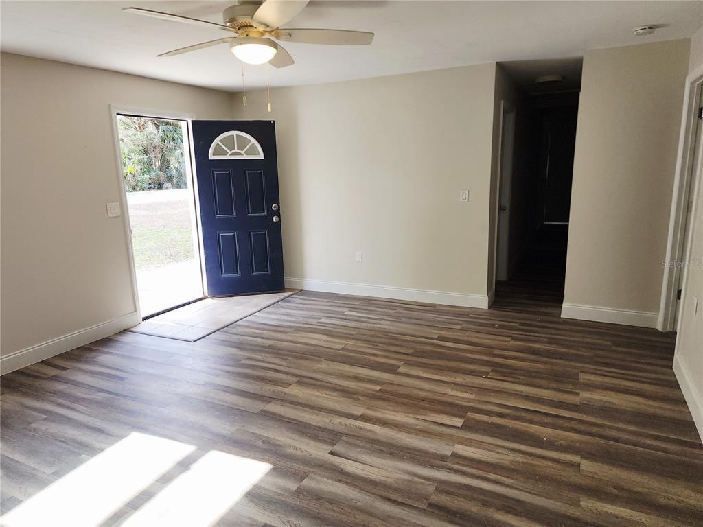 A room with wood-look flooring, a ceiling fan, and an open dark blue front door — 8150 SW 80TH TRAIL, TRENTON, FL