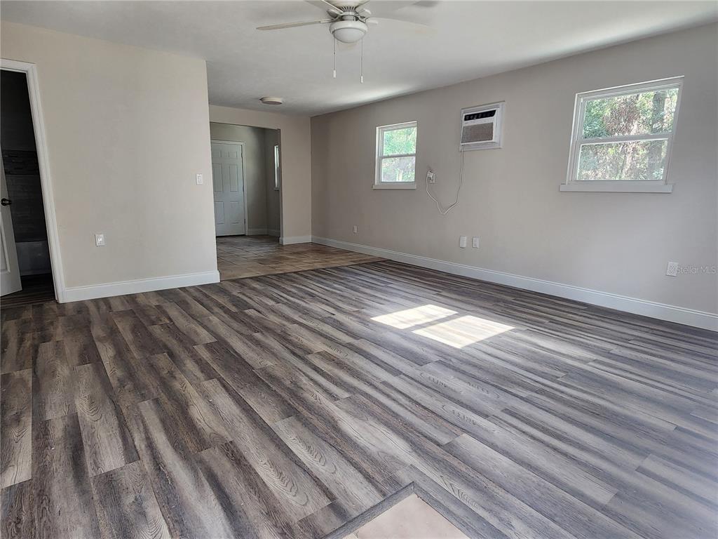 An empty living room features wood-look laminate flooring, light gray walls, and a ceiling fan — 8150 SW 80TH TRAIL, TRENTON, FL