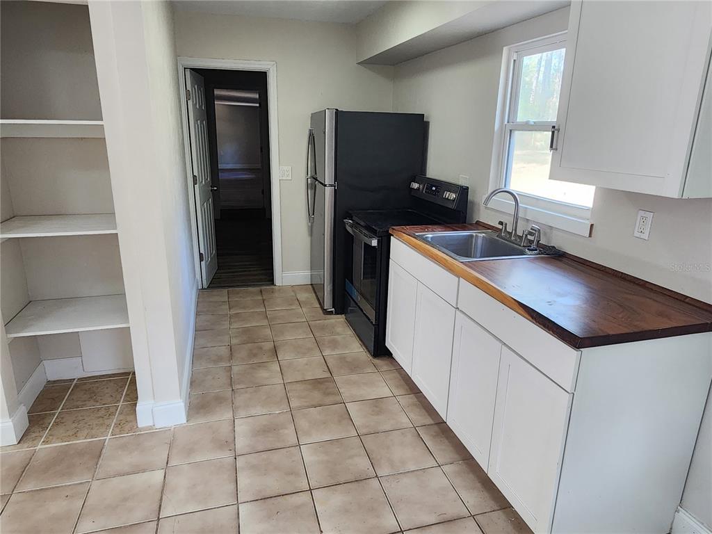 A kitchen features white cabinets, a wood countertop, a stainless steel sink, and tile flooring — 8150 SW 80TH TRAIL, TRENTON, FL
