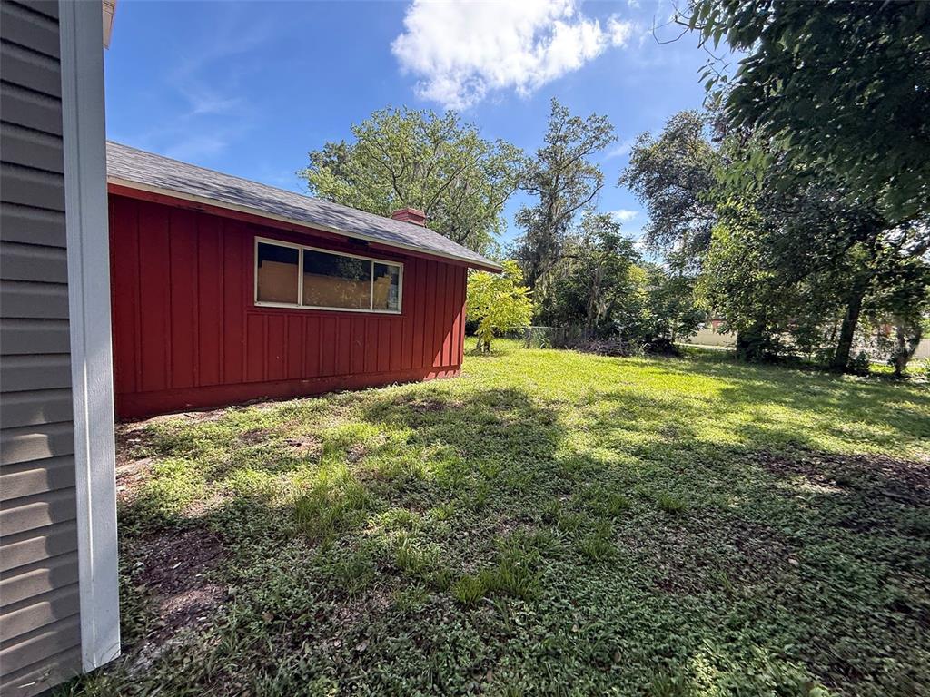A red exterior wall with a window stands beside a grassy yard under a blue sky — 2921 CRUTCHFIELD ROAD, LAKELAND, FL