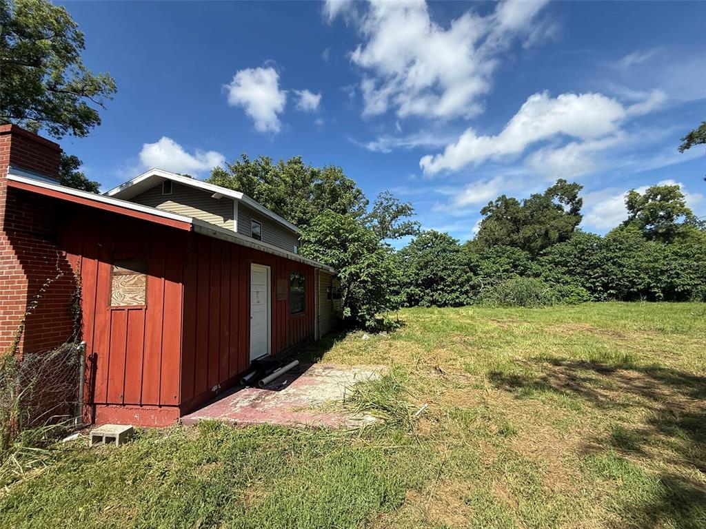 A red-sided house with a brick chimney and a concrete patio sits beside a field — 2921 CRUTCHFIELD ROAD, LAKELAND, FL