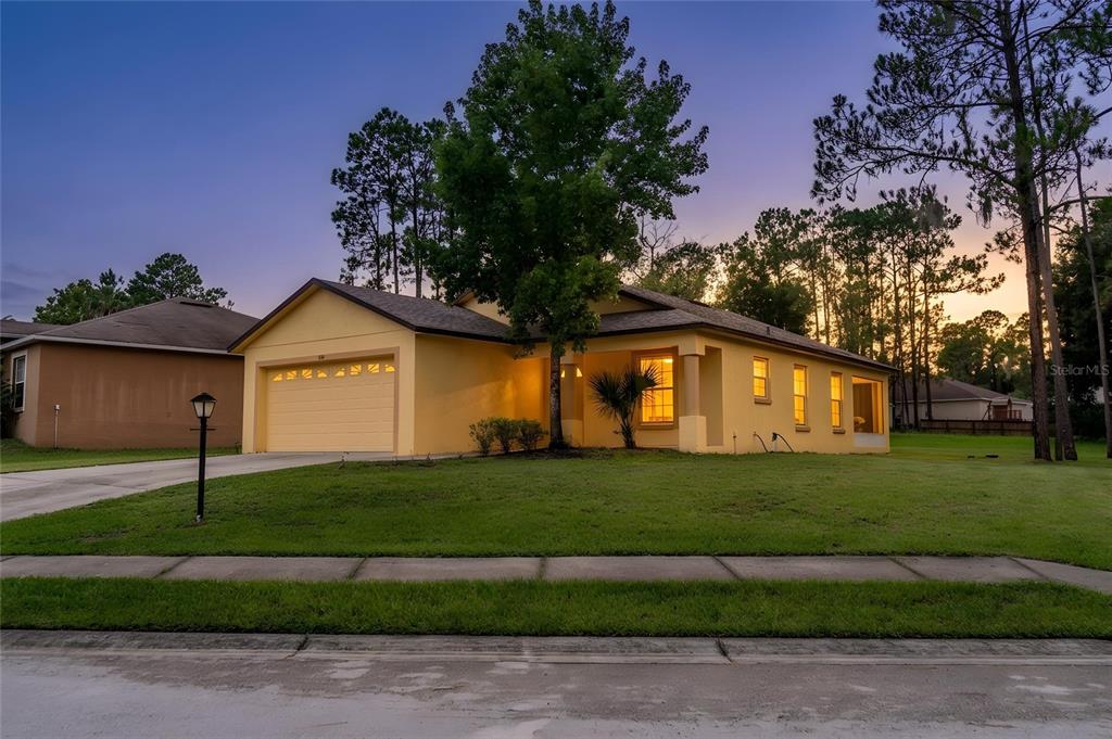 A yellow single-story house with a two-car garage sits on a grassy lot at dusk — 7941 SUGAR PINE BOULEVARD, LAKELAND, FL