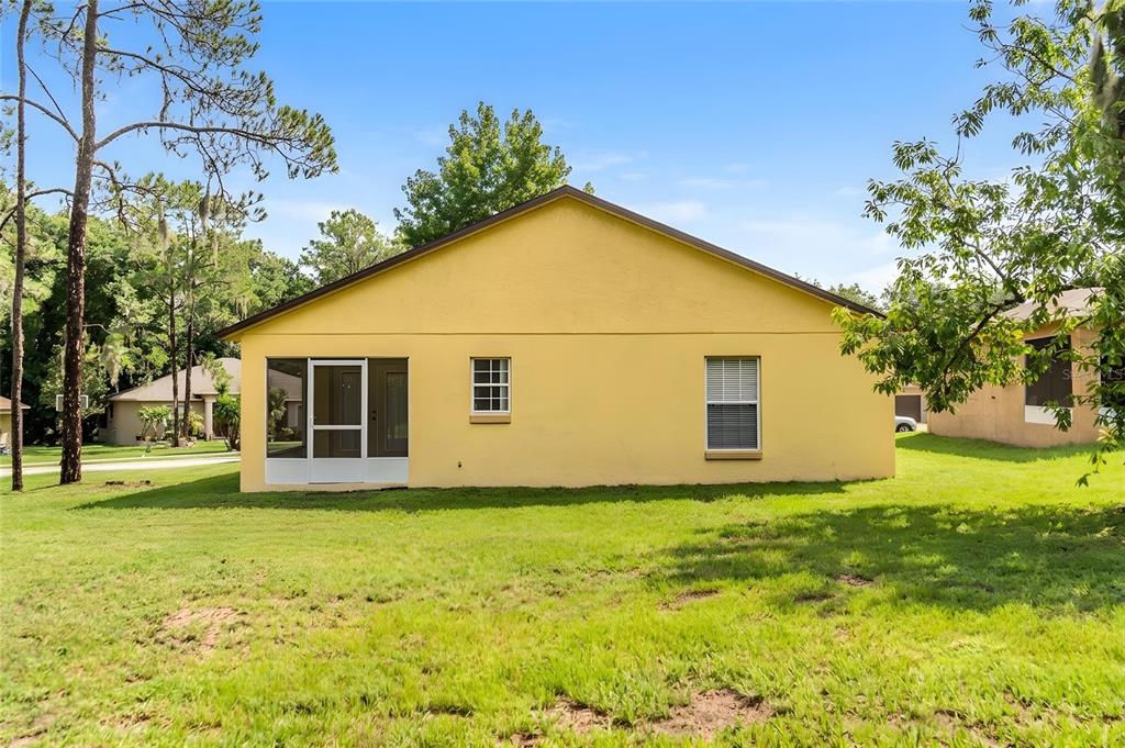 The exterior back view of a yellow house features a screened porch and two windows — 7941 SUGAR PINE BOULEVARD, LAKELAND, FL