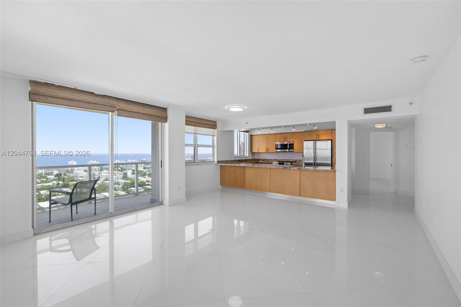 A bright open-concept living area features white tile floors, a kitchen with wood cabinets, and a balcony — 650 West Ave # 2912, Miami Beach FL 33139, MIAMI BEACH, FL