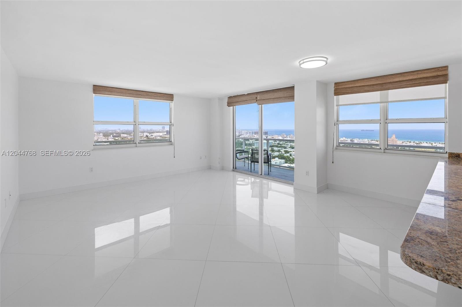 An empty living room features white tile floors, large windows, and a balcony with ocean views — 650 West Ave # 2912, Miami Beach FL 33139, MIAMI BEACH, FL