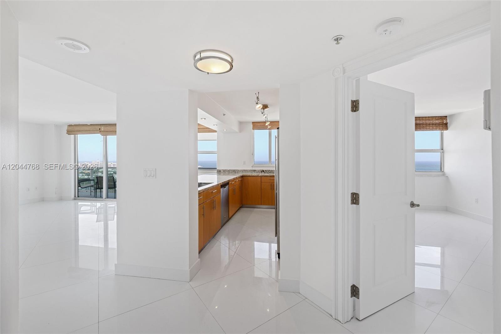 A kitchen with wood cabinets and granite countertops sits between two bright, white-tiled rooms — 650 West Ave # 2912, Miami Beach FL 33139, MIAMI BEACH, FL