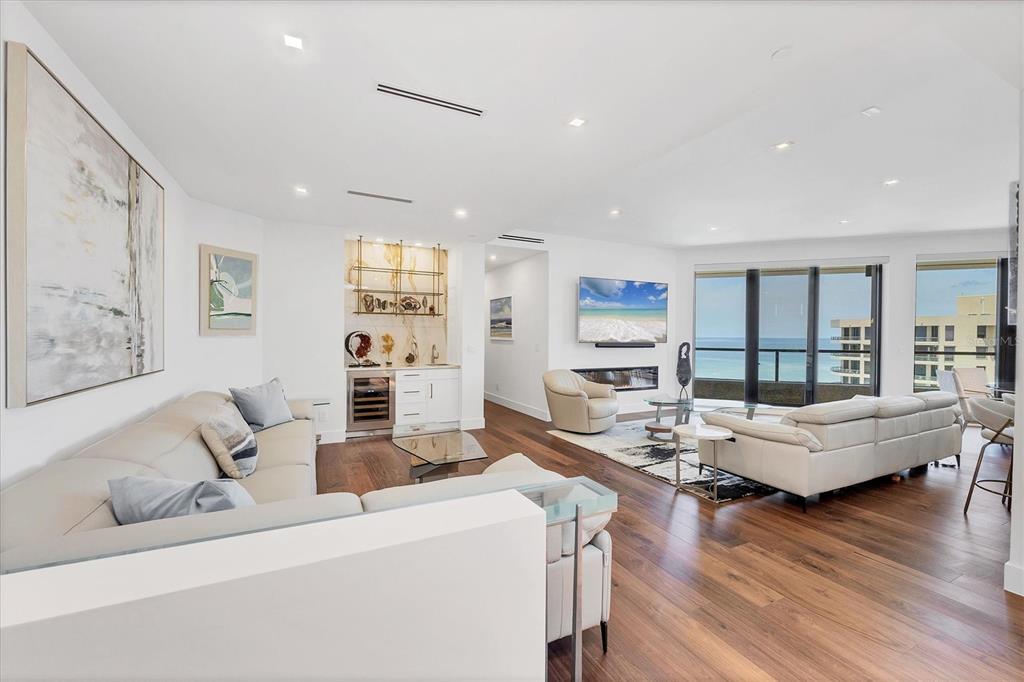 A modern living room features white sofas, a wet bar, and floor-to-ceiling windows overlooking the ocean — 1211 GULF OF MEXICO DRIVE UNIT 1005, LONGBOAT KEY, FL