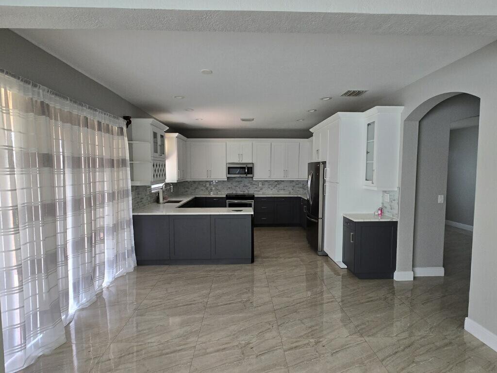 A modern kitchen features two-tone gray and white cabinetry, stainless steel appliances, and tiled flooring — 4436 Laurel Place, Weston FL 33332, WESTON, FL