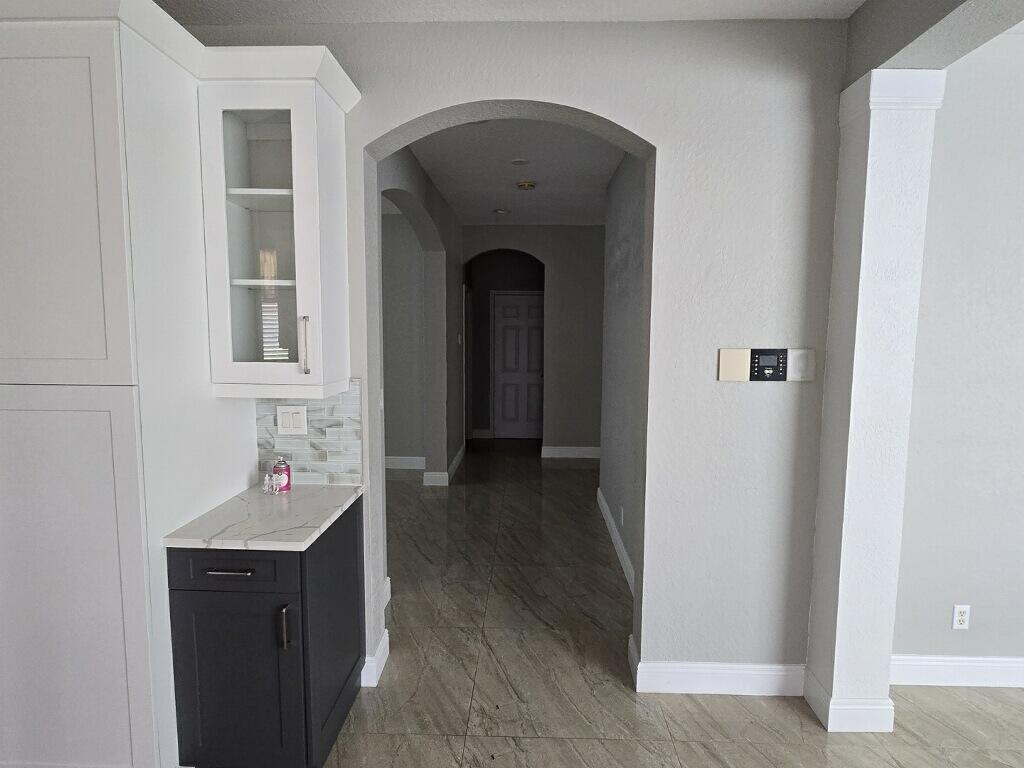 A dark cabinet with a marble countertop sits beside an arched hallway with tiled floors — 4436 Laurel Place, Weston FL 33332, WESTON, FL