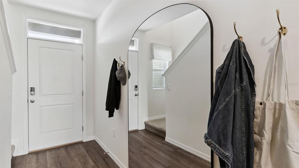 An entryway features a white door, wood-look flooring, a large arched mirror, and wall hooks — 4288 BUTTERSCOTCH CIRCLE, LAKELAND, FL