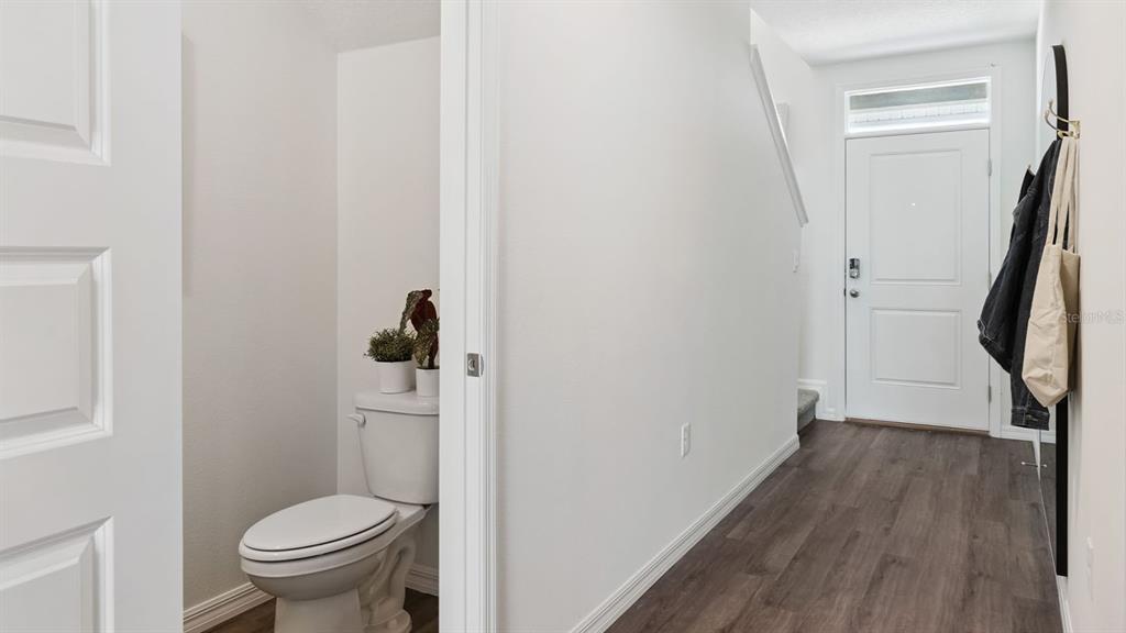 A hallway with dark wood-look flooring leads to a front door and a small bathroom — 4288 BUTTERSCOTCH CIRCLE, LAKELAND, FL