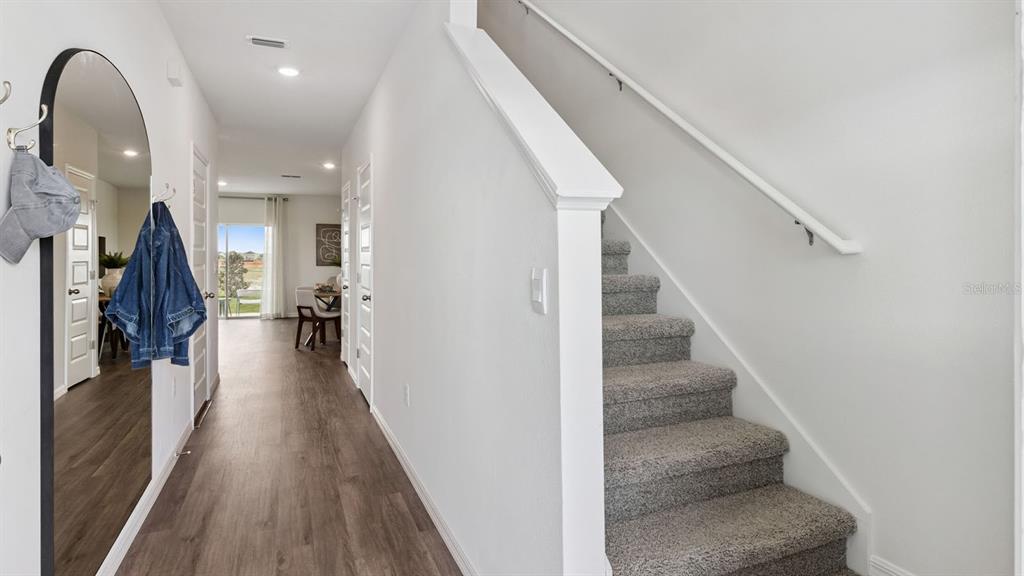 A hallway with wood-look flooring leads to a dining area, featuring stairs with carpeted steps — 4288 BUTTERSCOTCH CIRCLE, LAKELAND, FL