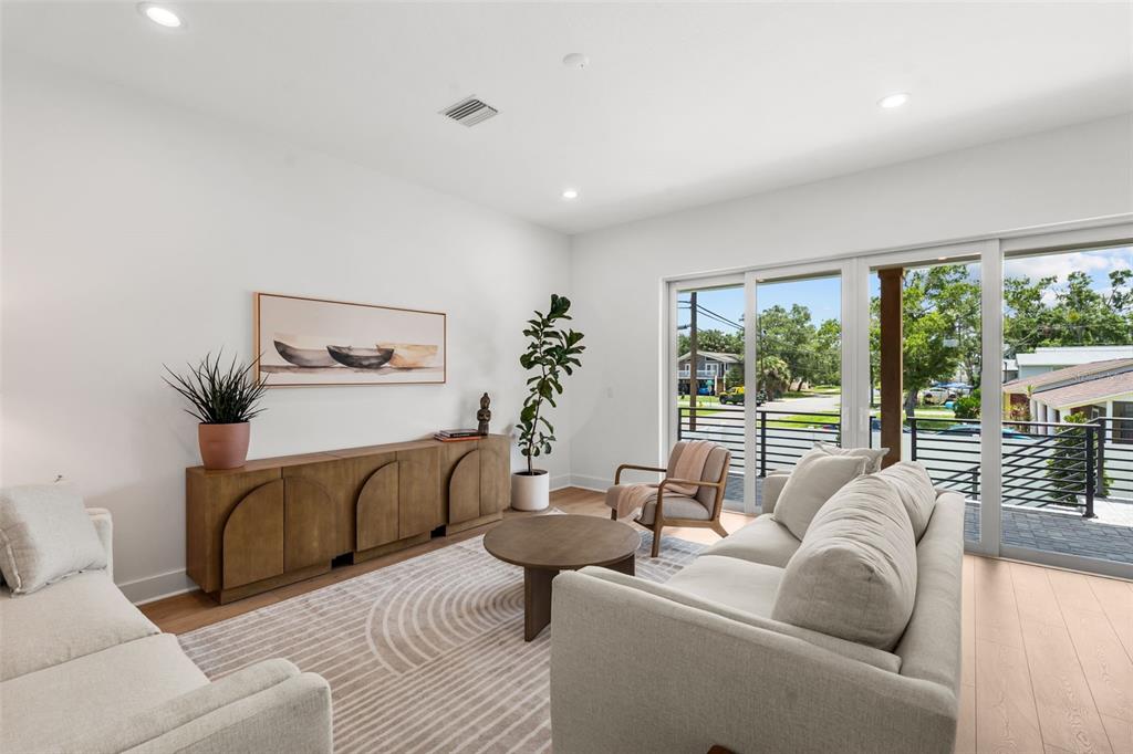 A modern living room features a light-colored sofa, wooden sideboard, and sliding glass balcony doors — 7402 S SWOOPE STREET, TAMPA, FL
