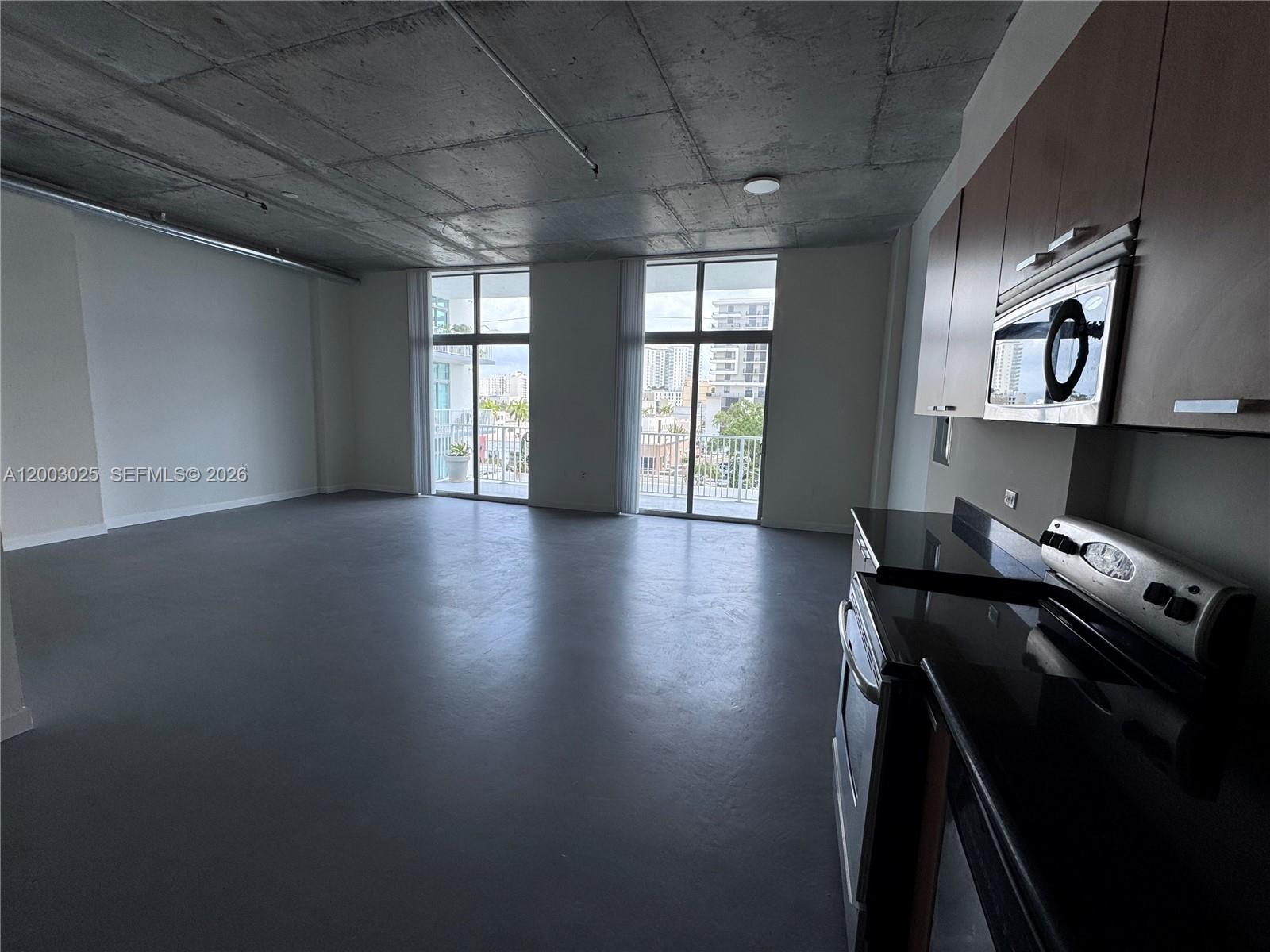 An open-concept apartment features a concrete ceiling, gray flooring, and a kitchen with dark countertops — 2100 Van Buren St # 412, Hollywood FL 33020, HOLLYWOOD, FL
