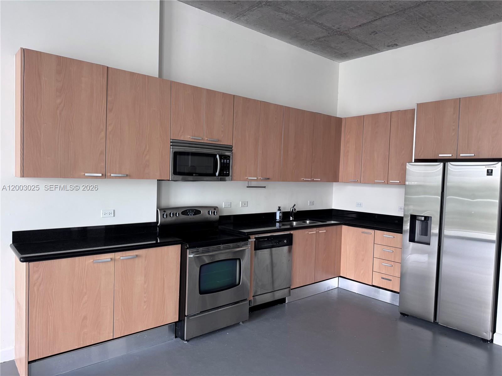 A kitchen features light wood cabinets, black countertops, stainless steel appliances, and a concrete ceiling — 2100 Van Buren St # 412, Hollywood FL 33020, HOLLYWOOD, FL