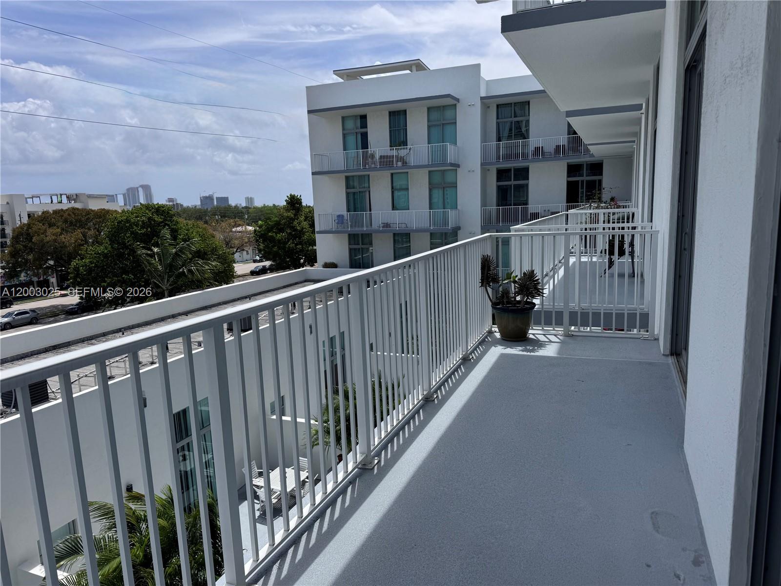 A balcony with white railings overlooks a neighboring apartment building and a distant city skyline — 2100 Van Buren St # 412, Hollywood FL 33020, HOLLYWOOD, FL