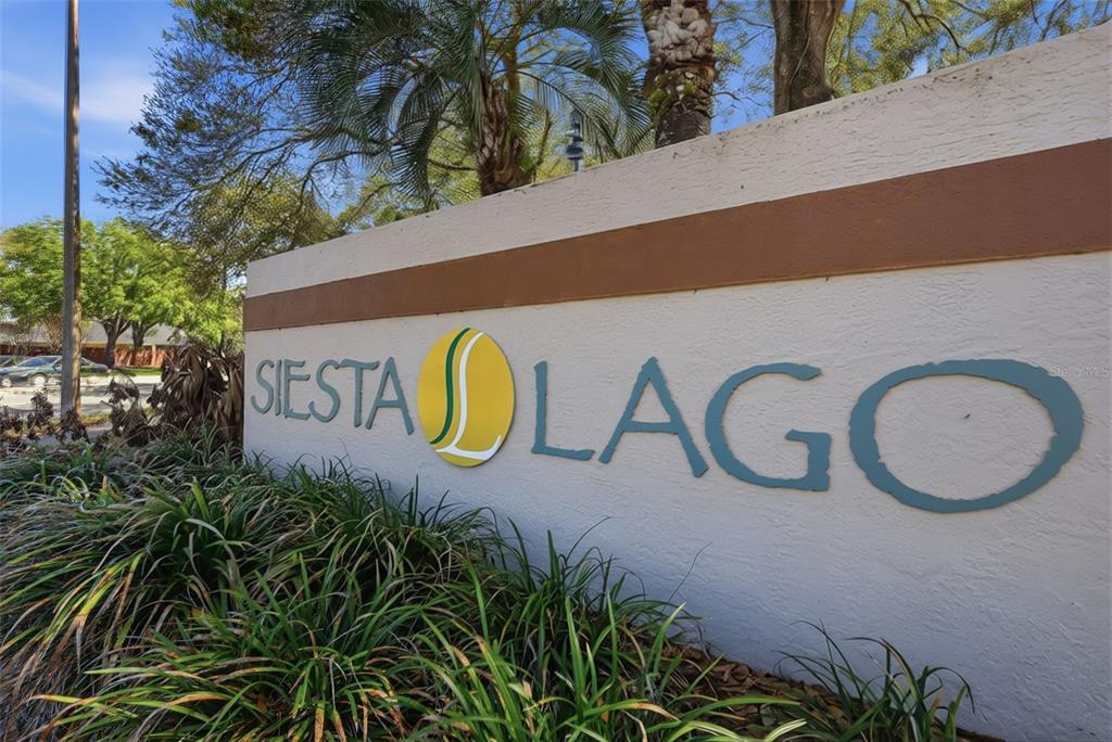 A beige stucco sign with the name Siesta Lago stands outdoors near green landscaping — 5452 E MICHIGAN STREET UNIT 5452-7, ORLANDO, FL